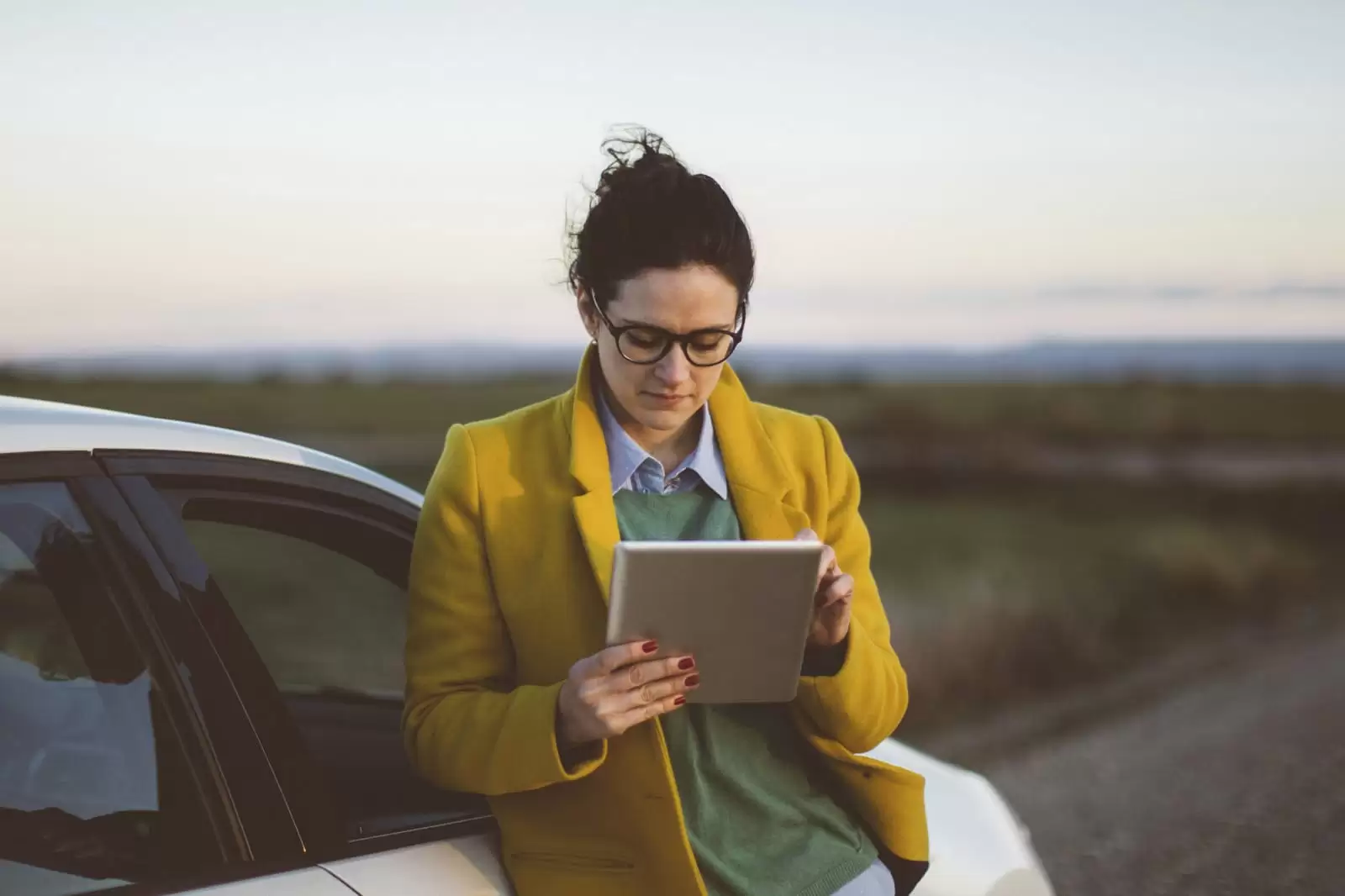 Una chica apoyada en un coche consultando sobre seguro de automóvil en una tablet