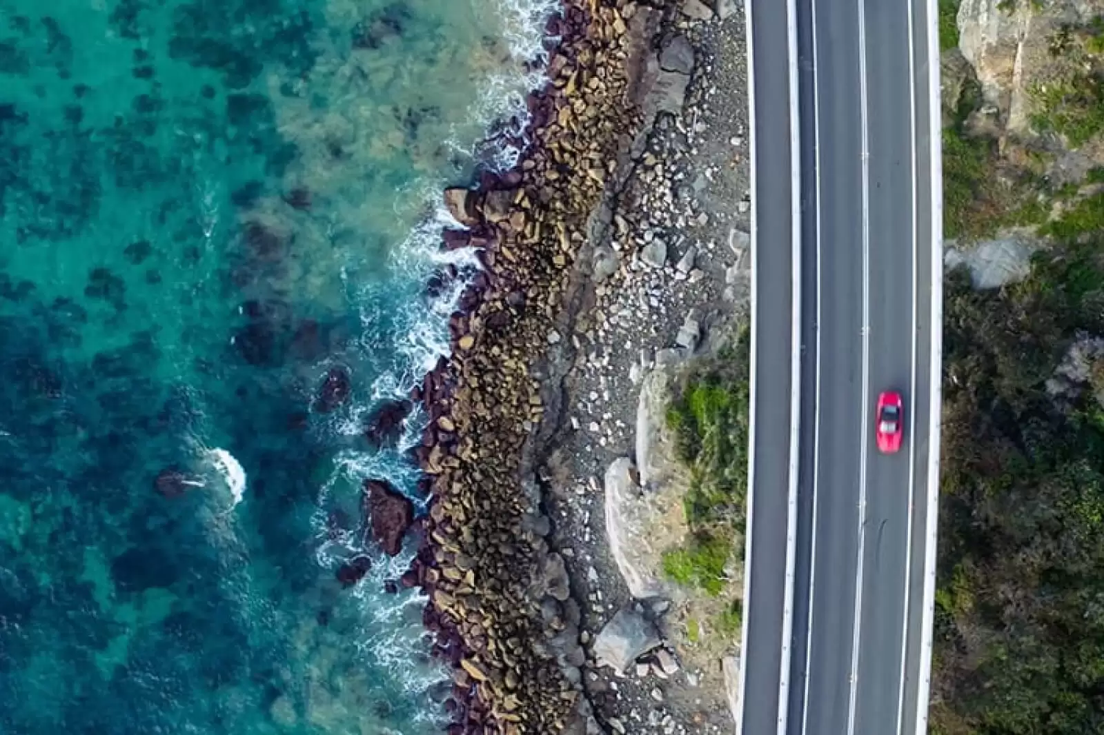 Un coche del Grupo Volkswagen, rojo, en una carretera junto al mar visto desde arriba 